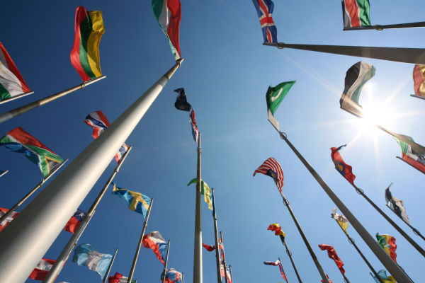 Flags from different countries waving against a bright blue sky